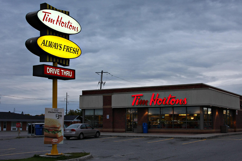 Photo of Tim Hortons restaurant with big sign in front and cloudy sky in background