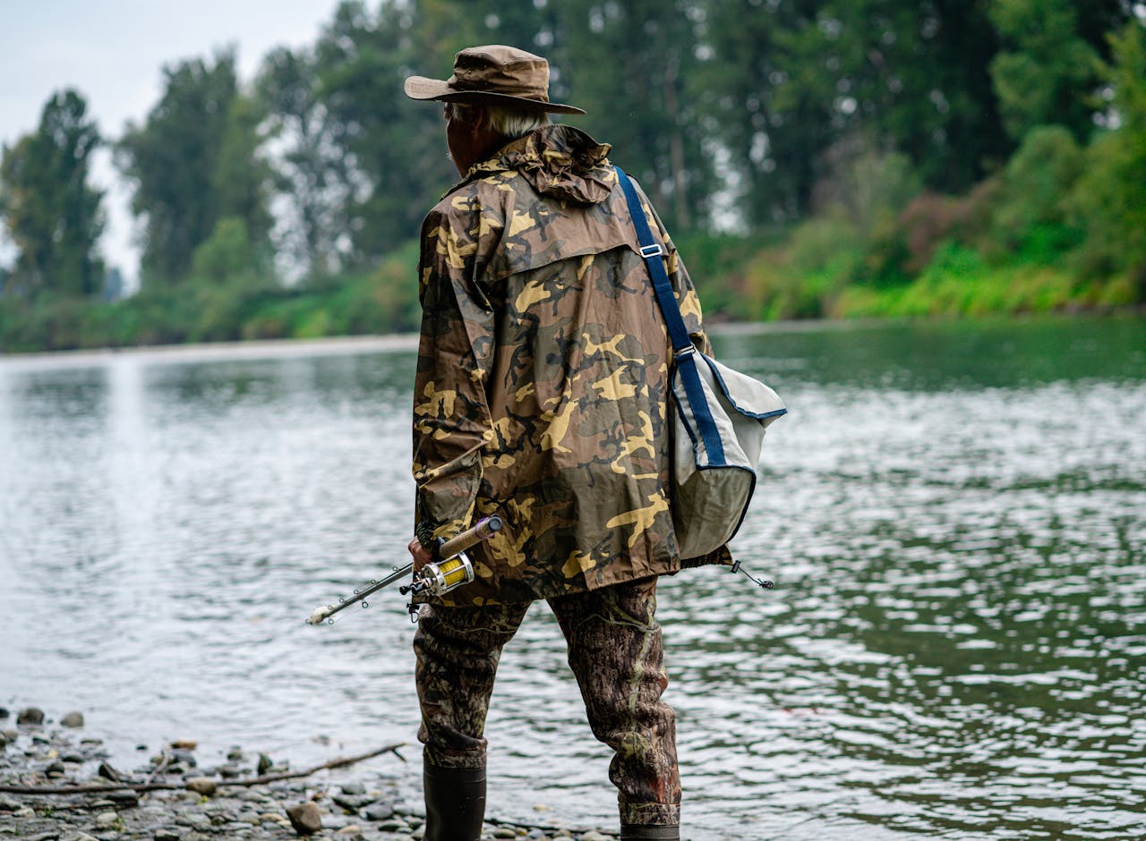 Man in Camouflage Top and Pants Walking on Shore with Fishing Rod