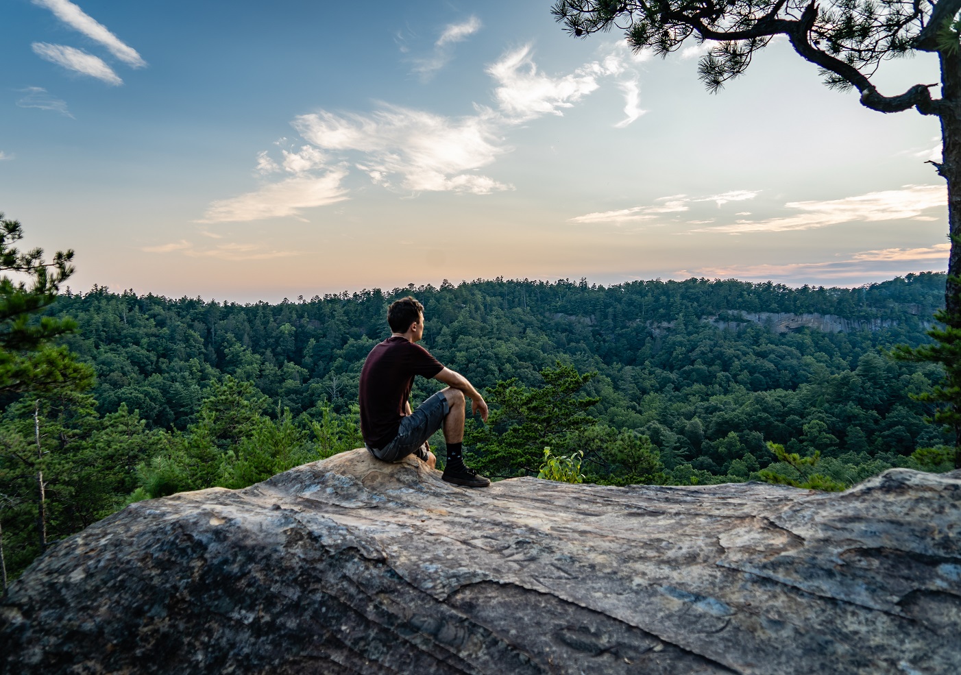 A young man sits on an outcropping of rock atop a mountain in Red River Gorge, Daniel Boone National Forest, Kentucky.
