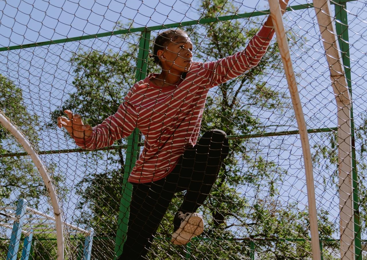 A Kid Climbing a Wire Fence.