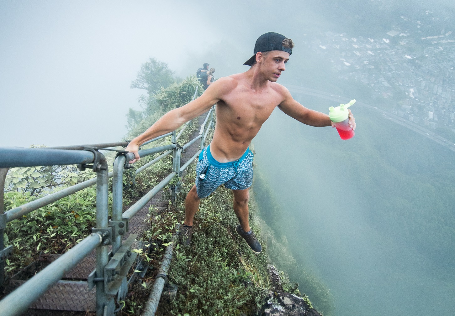 Fit man standing on the edge of cliff holding onto stairs.