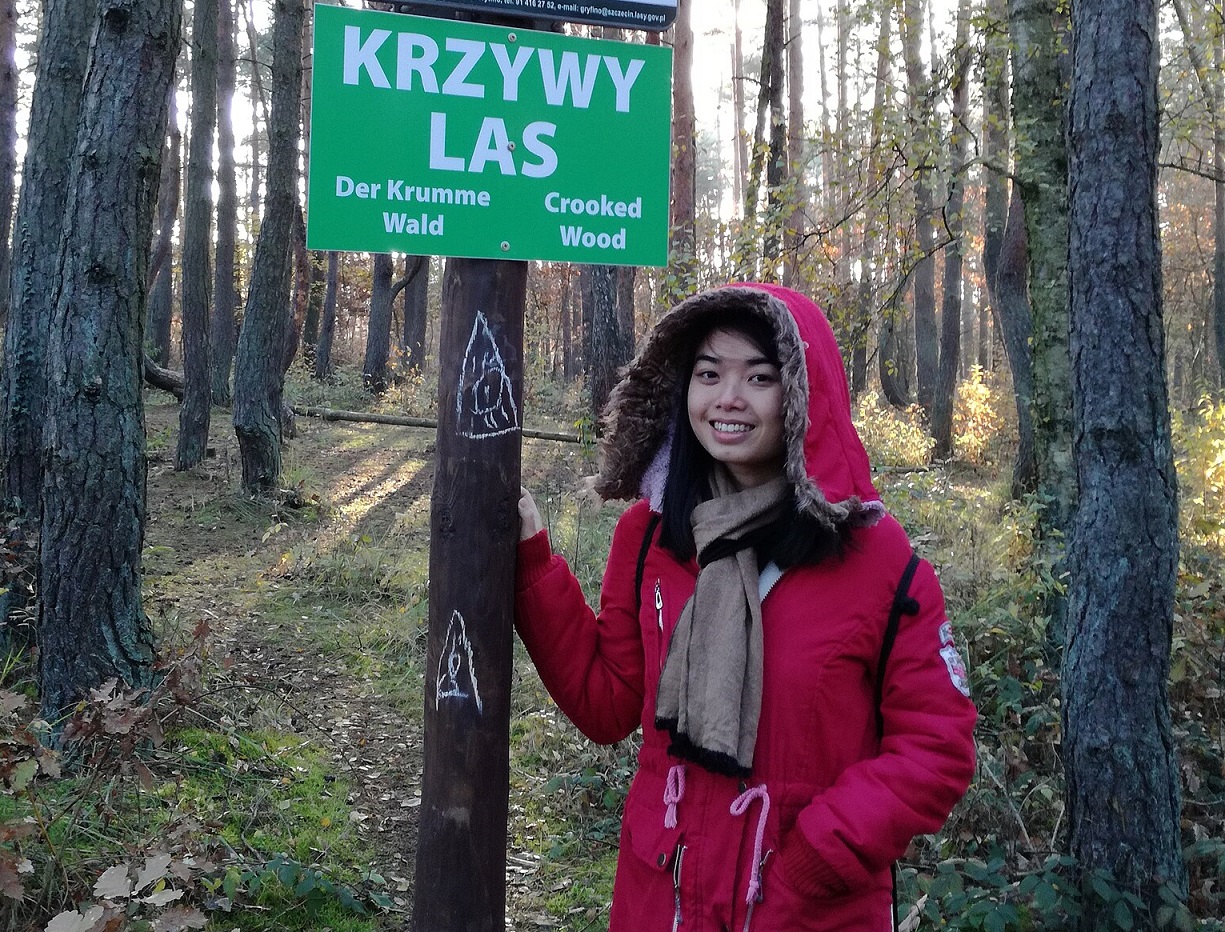 Woman standing next to a sign in Crooked wood (Krzywy Las) - Gryfino, Poland.
