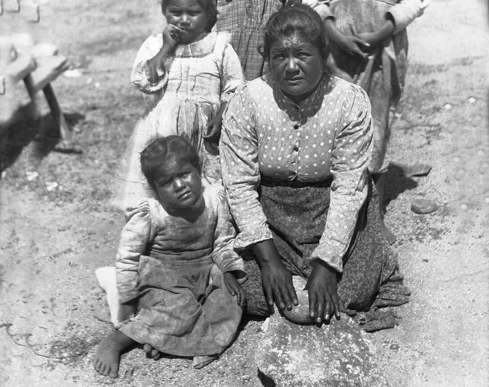 Photograph of a woman and her kids using stones for grinding
