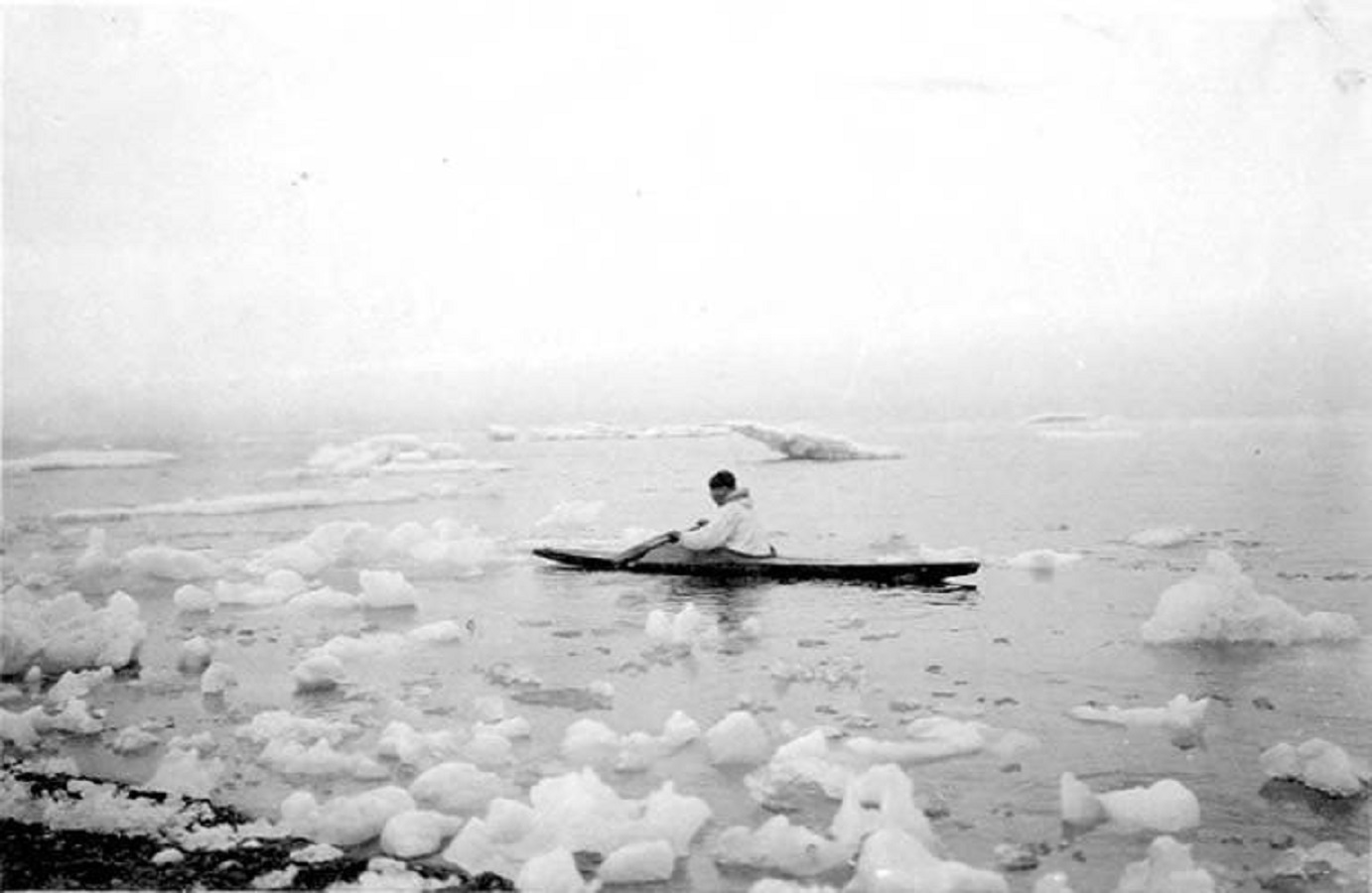 Eskimo man paddling kayak among chunks of ice