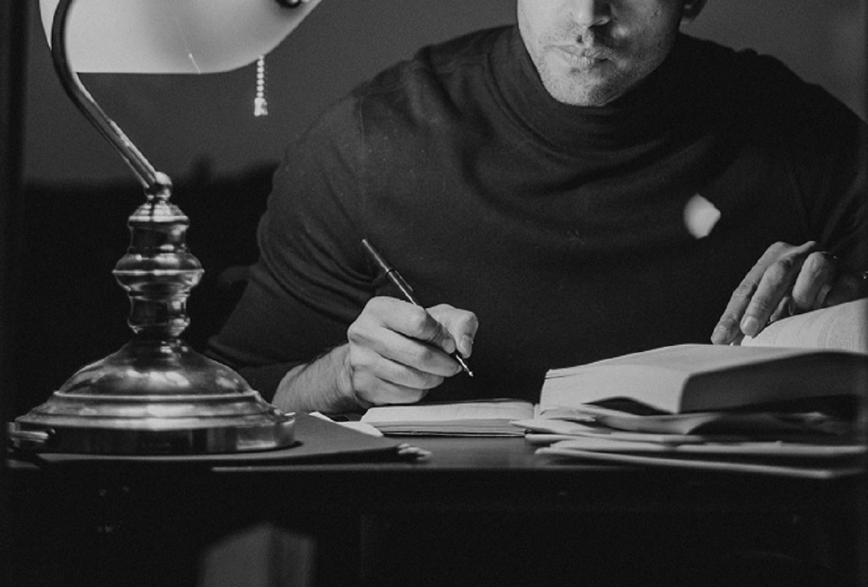 Man reading book and taking notes in home office.