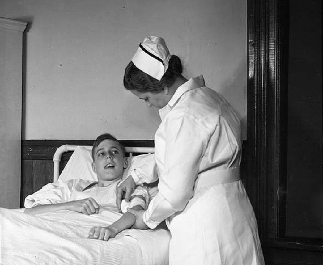 Young man in an hospital bed getting bandaged up by a nurse.
