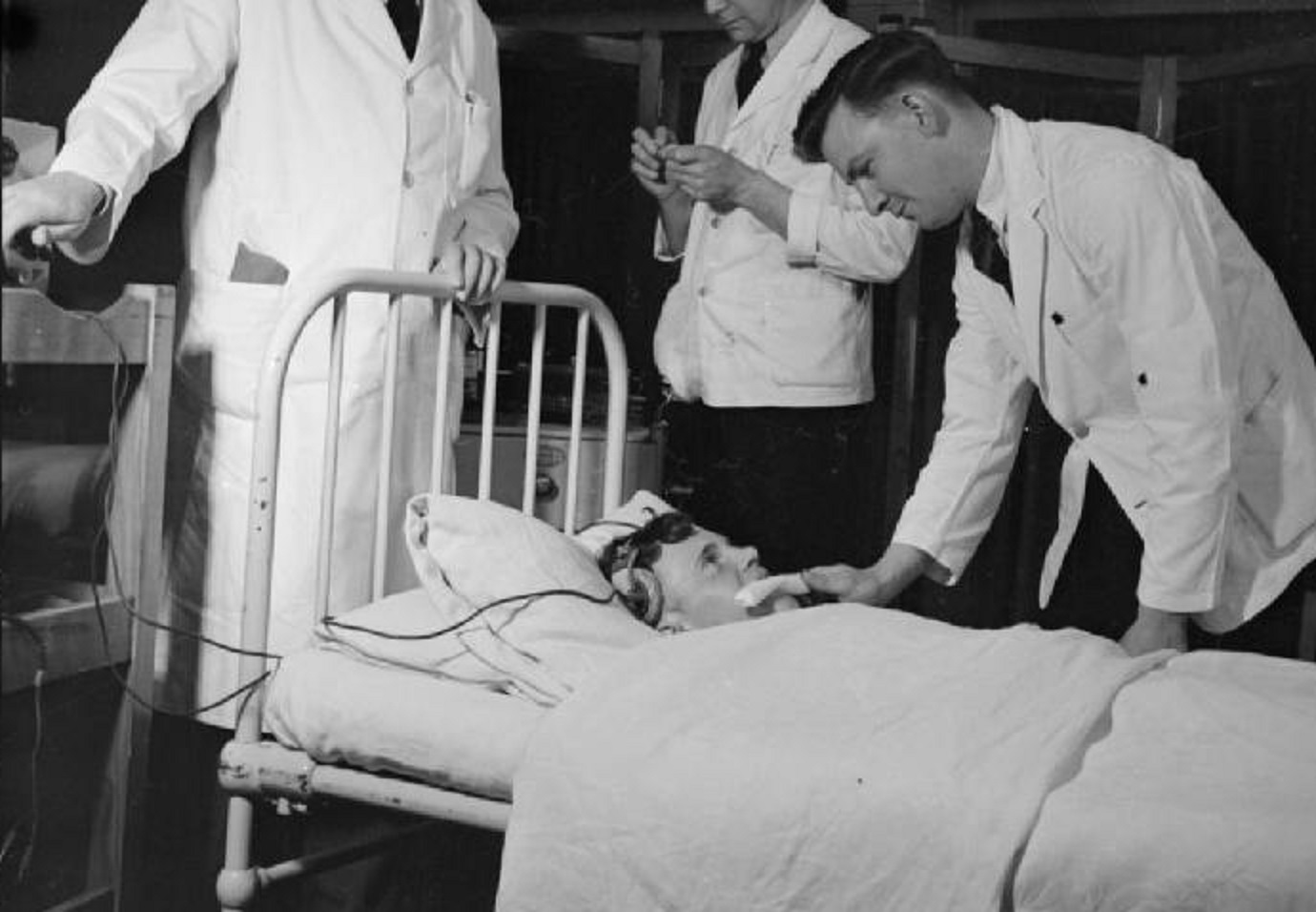 A male inserts a gag into a patient's mouth as the doctor (left) prepares to begin Convulsant Therapy treatment.
