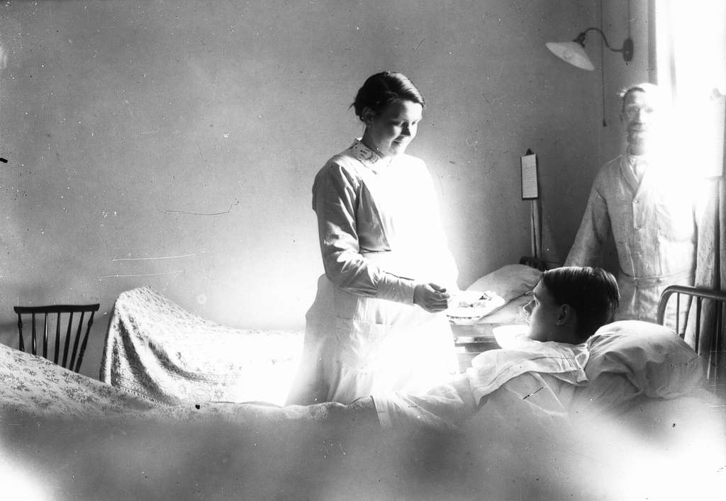Patient in hospital bed next to a nurse.