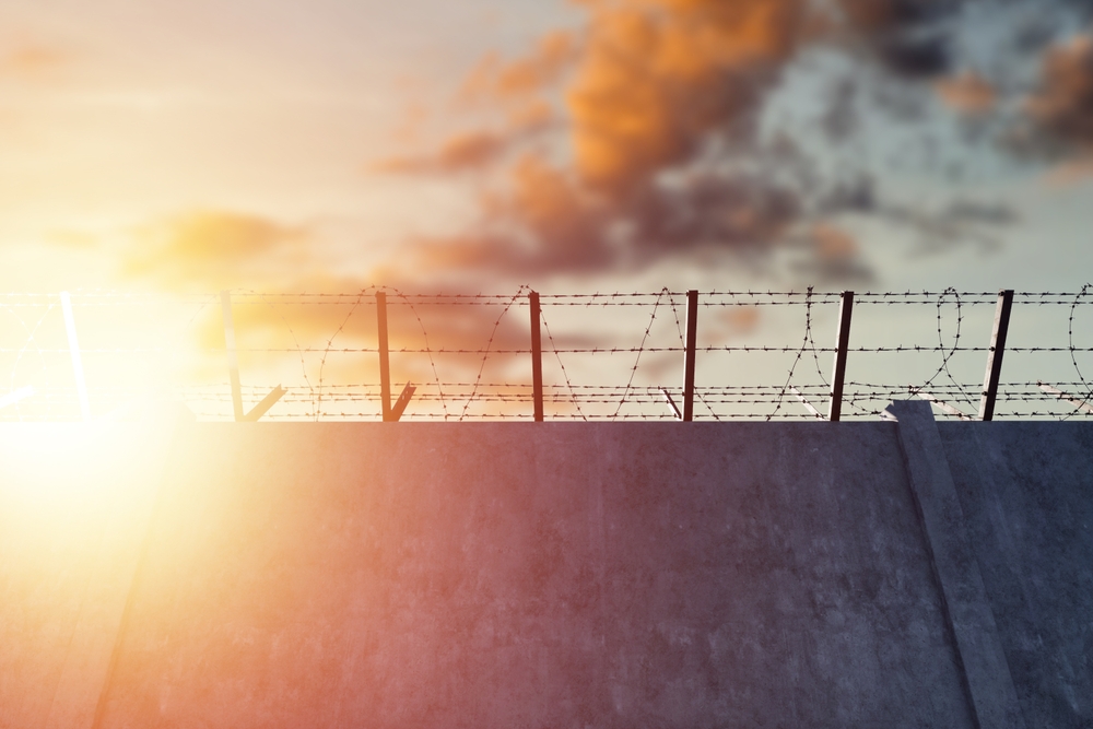 Concrete wall with barbed wire against blue sky