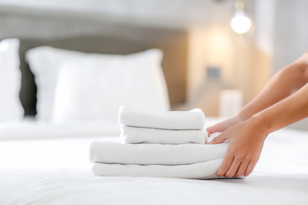 Close-up of hands putting stack of fresh white bath towels