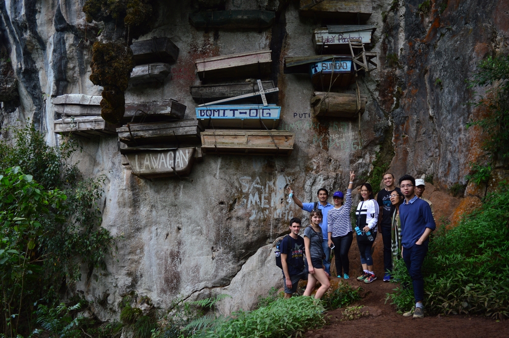 tourists photograph historic hanging coffins suspended from cliffs
