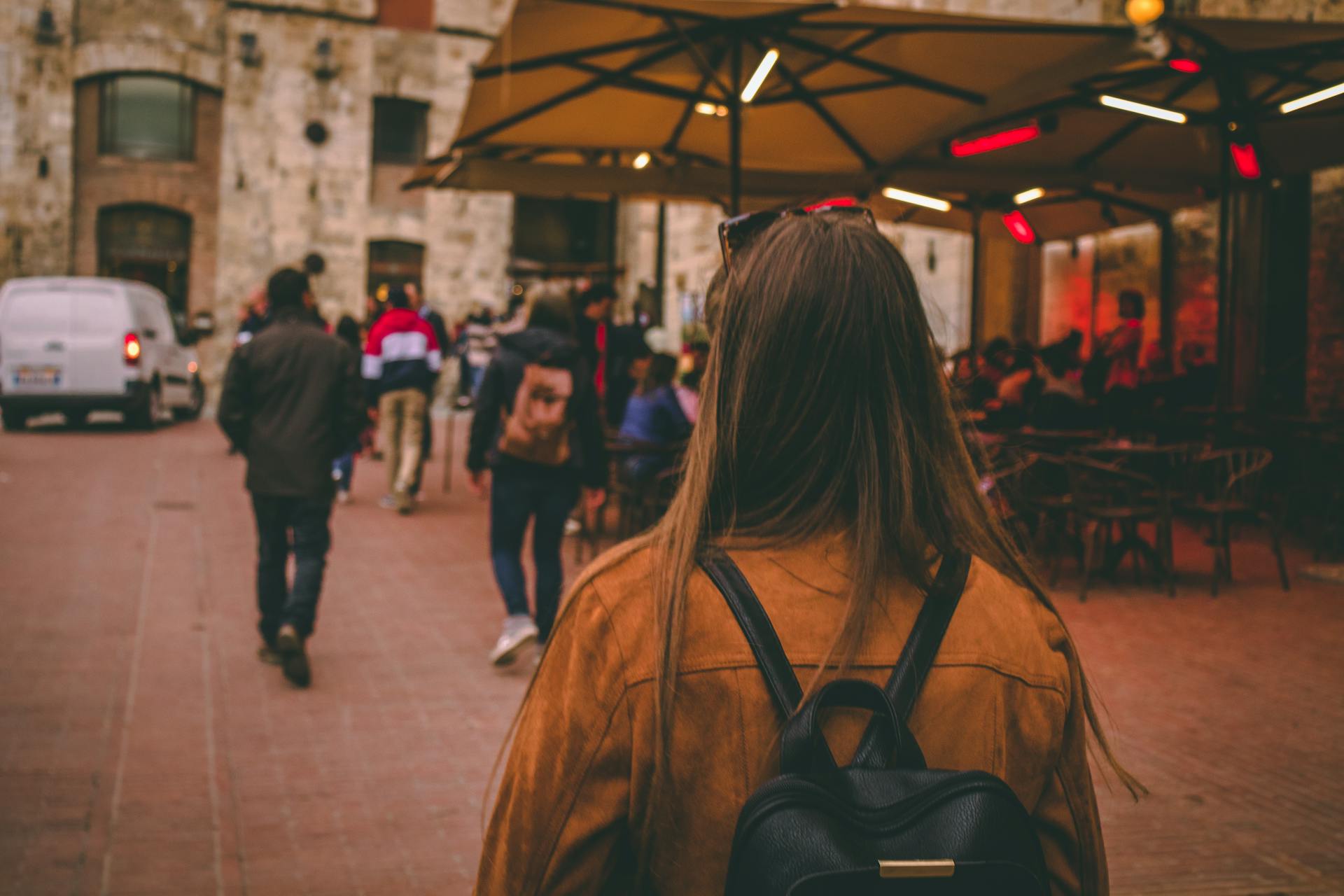 Woman tourist in brown jacket and backpack walking on a busy street