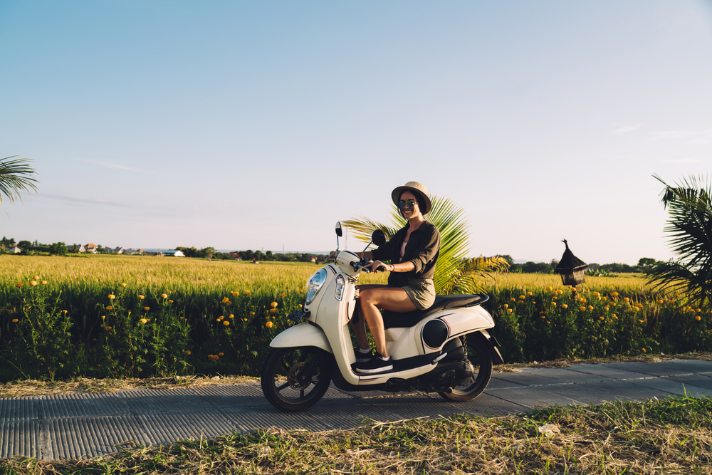 Portrait of cheerful female tourist sitting on rented vintage moped
