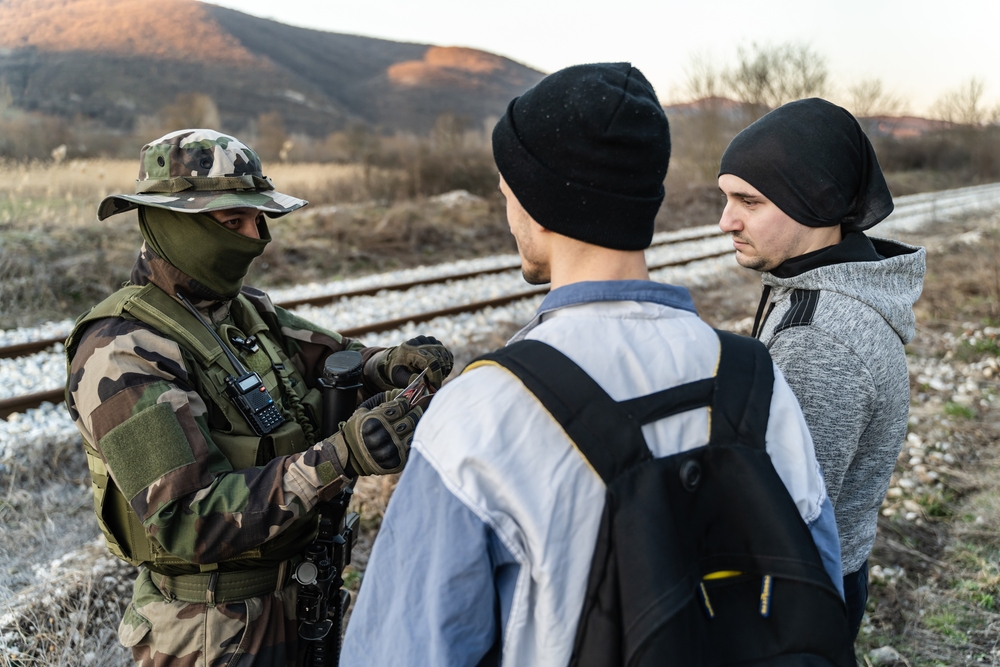 Armed soldier in uniform checking documents of suspect migrant