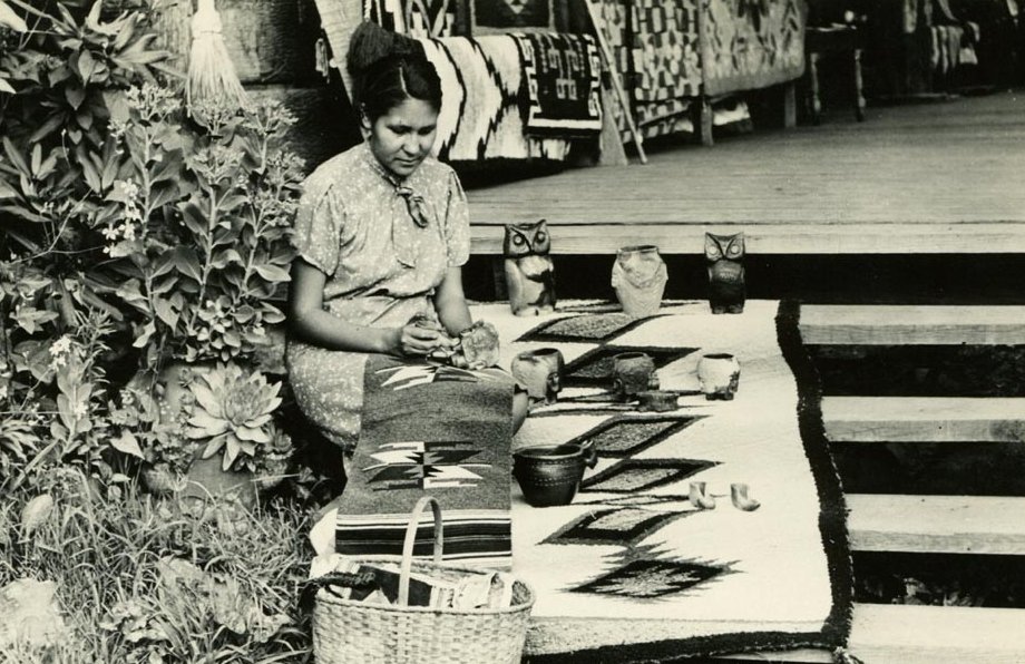 Grayscale Portrait Photo of a woman sitting next to a display of pottery