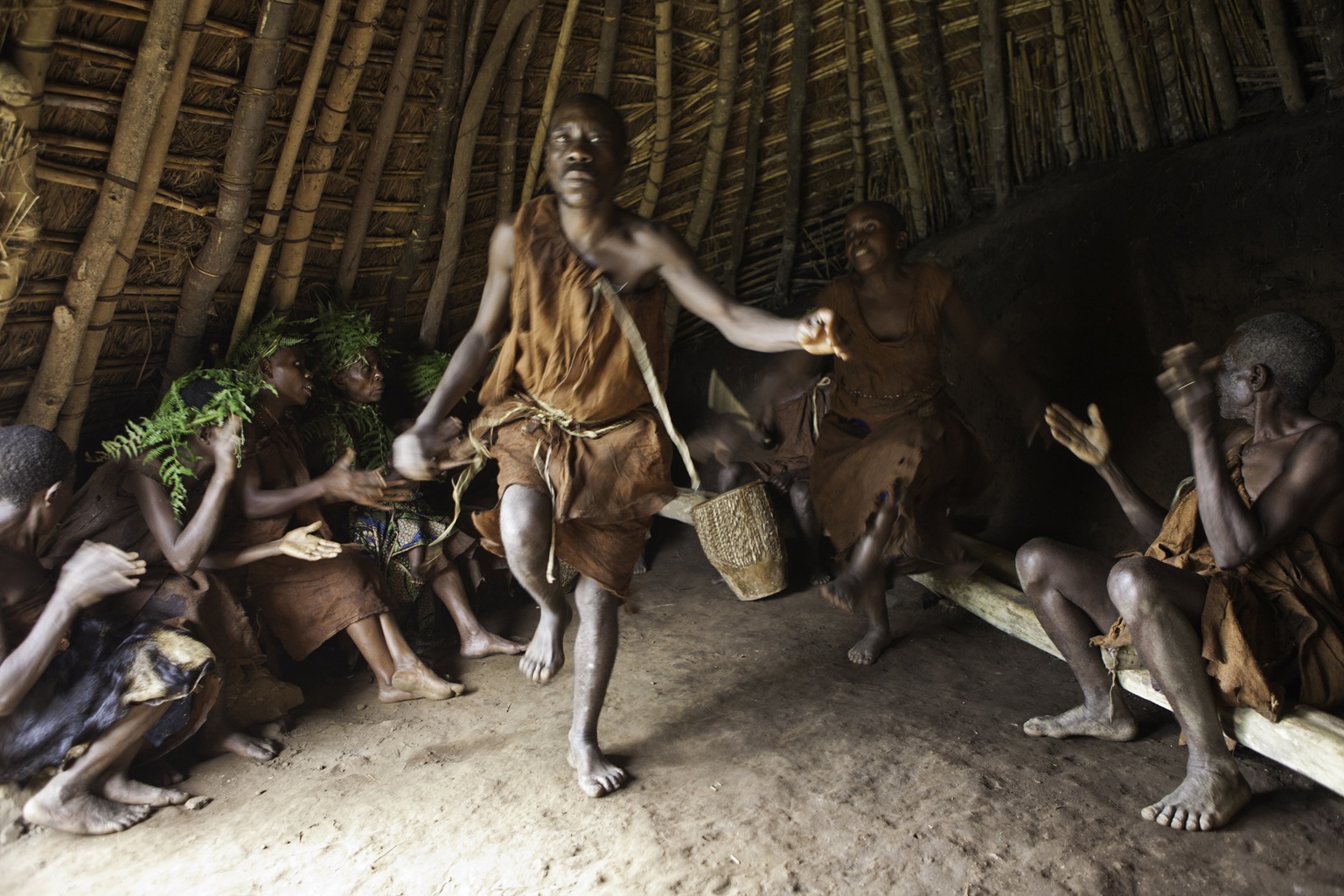 Batwa members act out a story with music song and dance in the village house of Mukuno