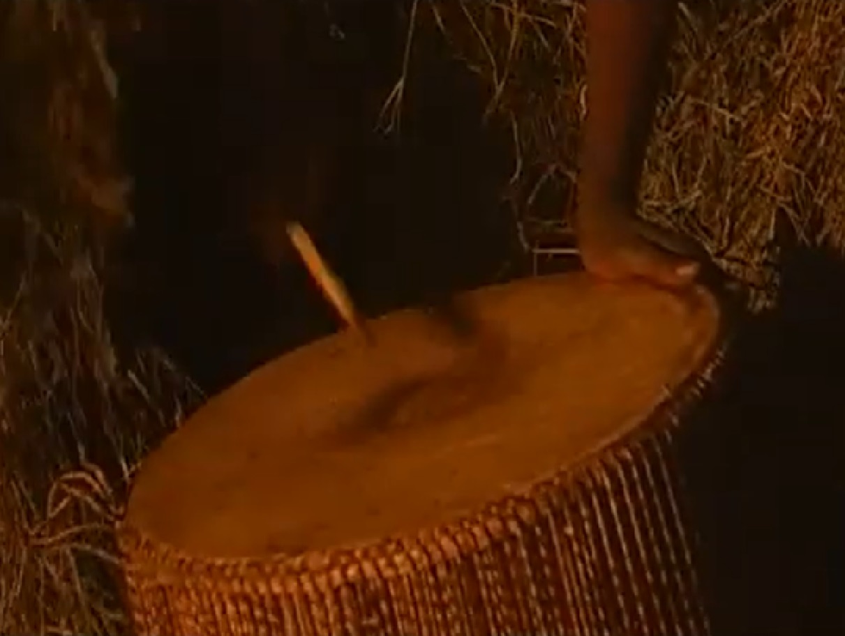 Screenshot of Batwa tribe man hitting on a drum to celebrate - from The Batwa Legacy (2011)