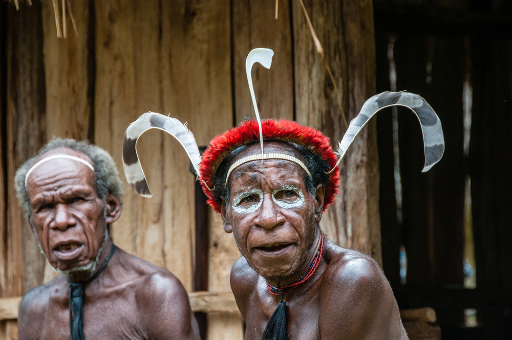 a headmaster Dani shows a traditional hairstyle with feathers and tribal colors on face