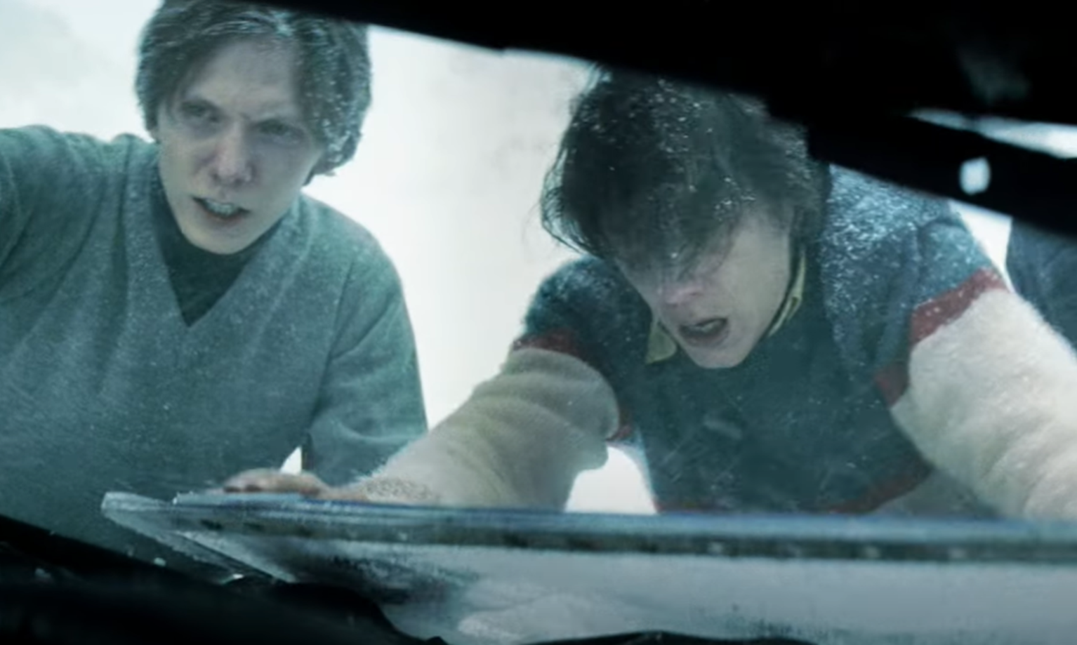 Screenshot of man helping injured people in the snow - from Society of the Snow (2023)