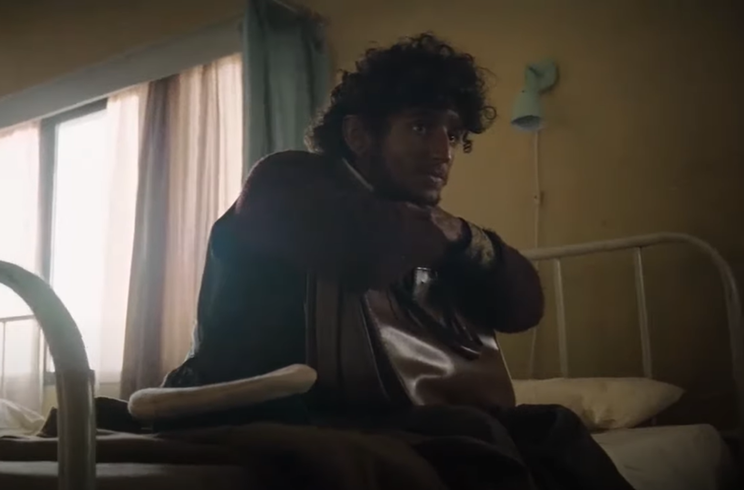 Screenshot of survivor from Flight 571 seating on the hospital bed - from Society of the Snow (2023)