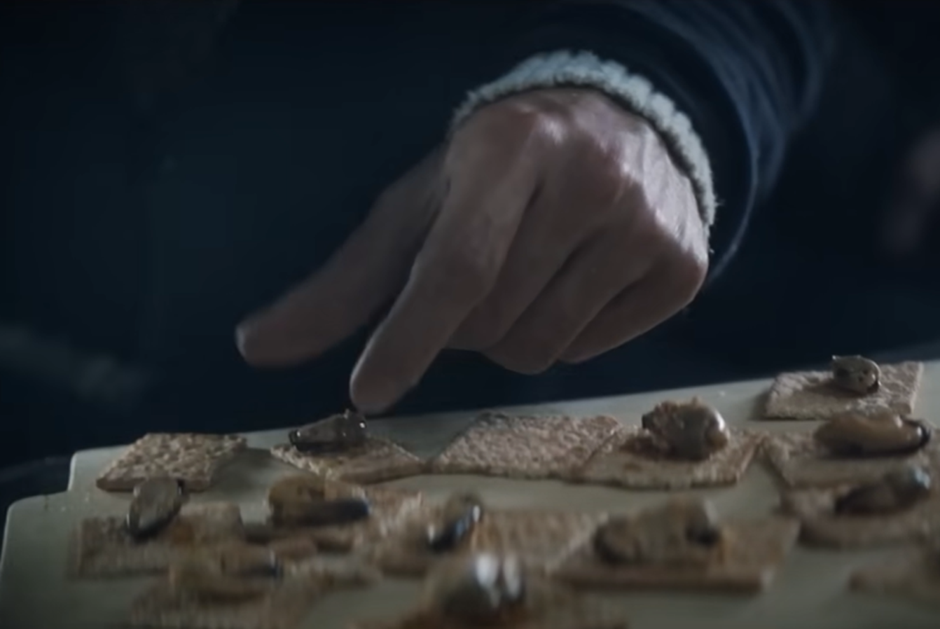 Screenshot of man making food for other people outside - from Society of the Snow (2023)