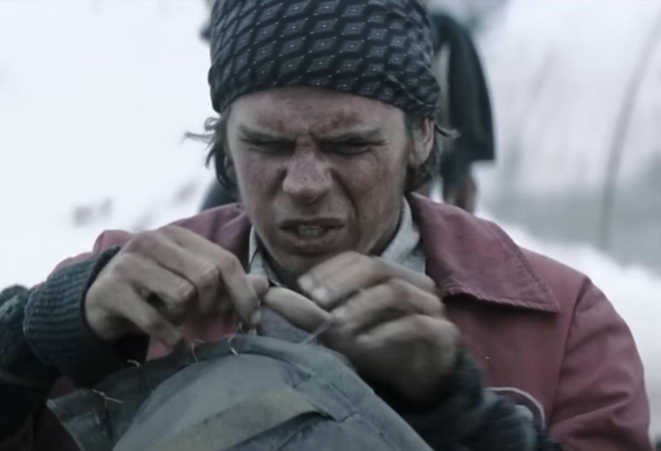 Screenshot of man making sleeping bag outside - from Society of the Snow (2023)