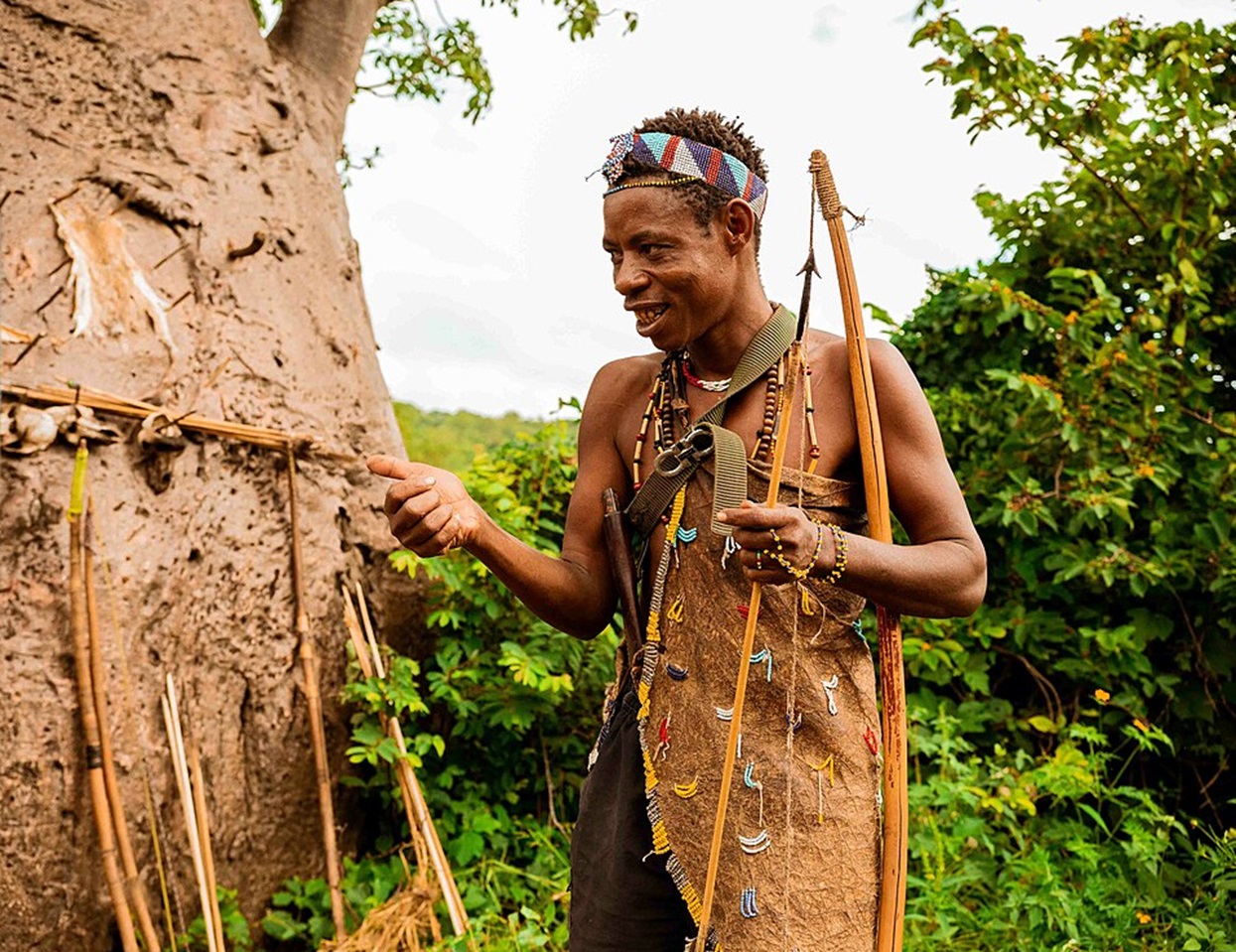 A Hunter With His Instruments Next To A Tree In A Bush In Tanzania