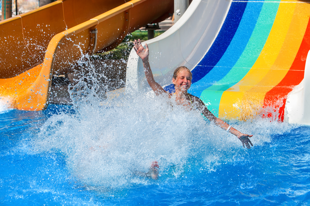 Happy kid on water slide at water park hands up