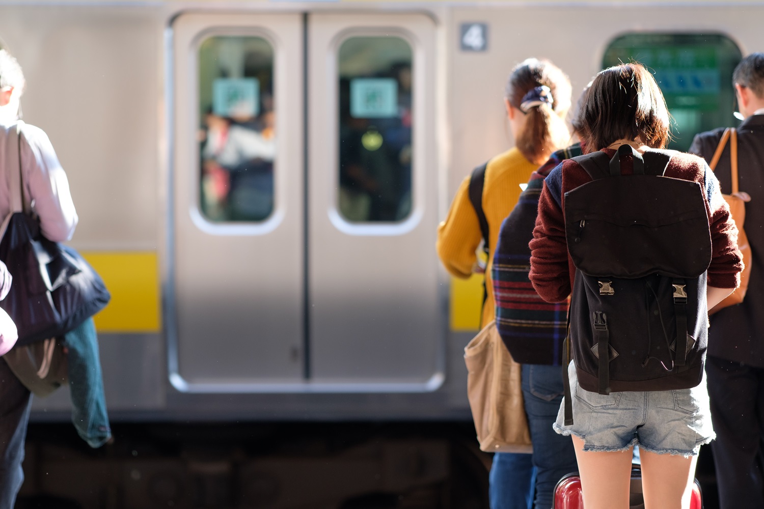 Young Japanese woman hunched over her phone while waiting for her train in a railway station in Tokyo.