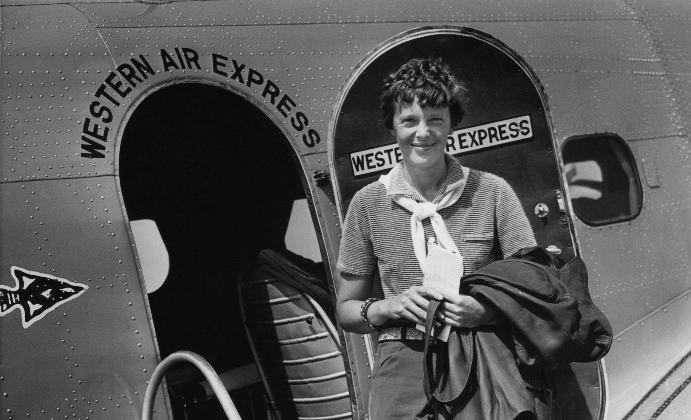 Amelia Earhart standing in front of a door of a plane