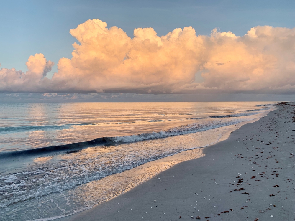 A picturesque beach scene with calm waters of Sanibel Island and fluffy white clouds.