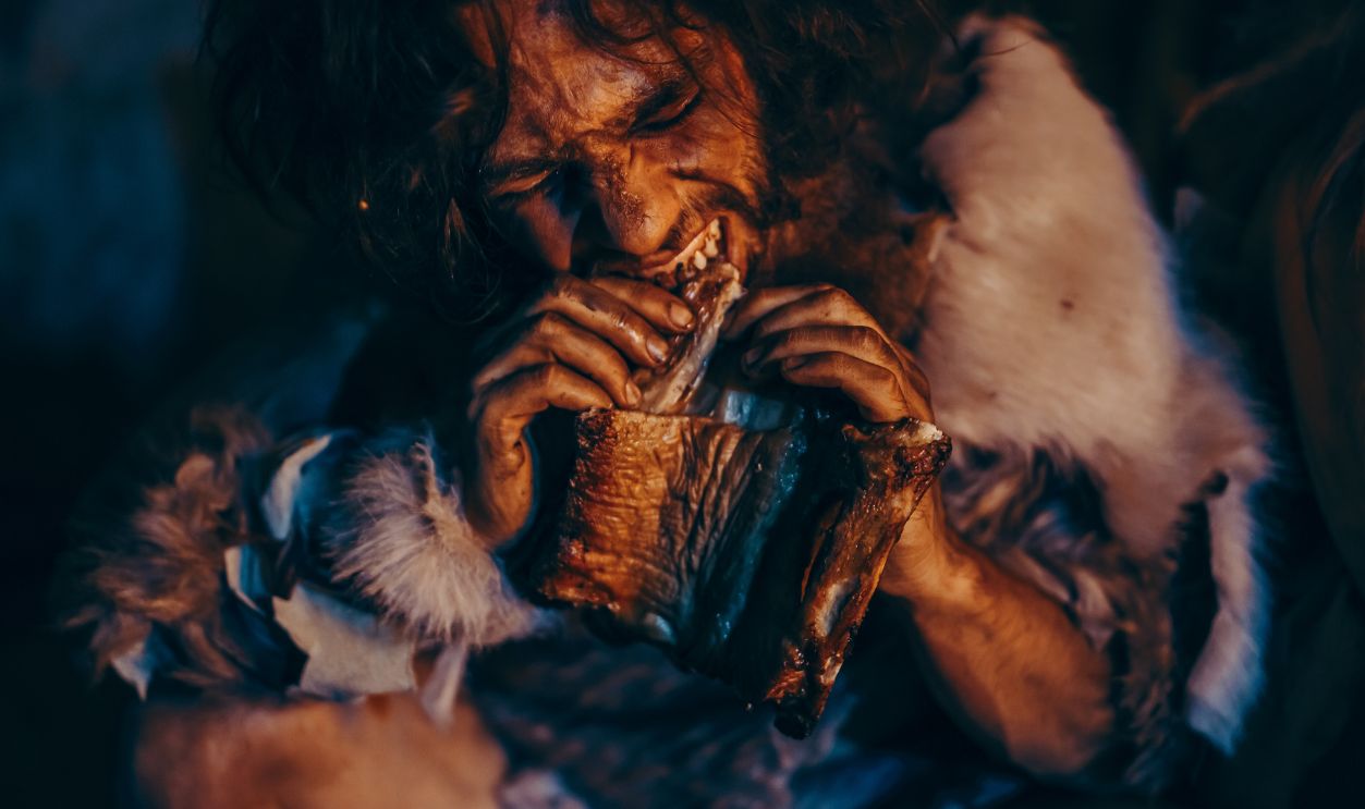 Neanderthal or Homo Sapiens Family Cooking Animal Meat over Bonfire and then Eating it.