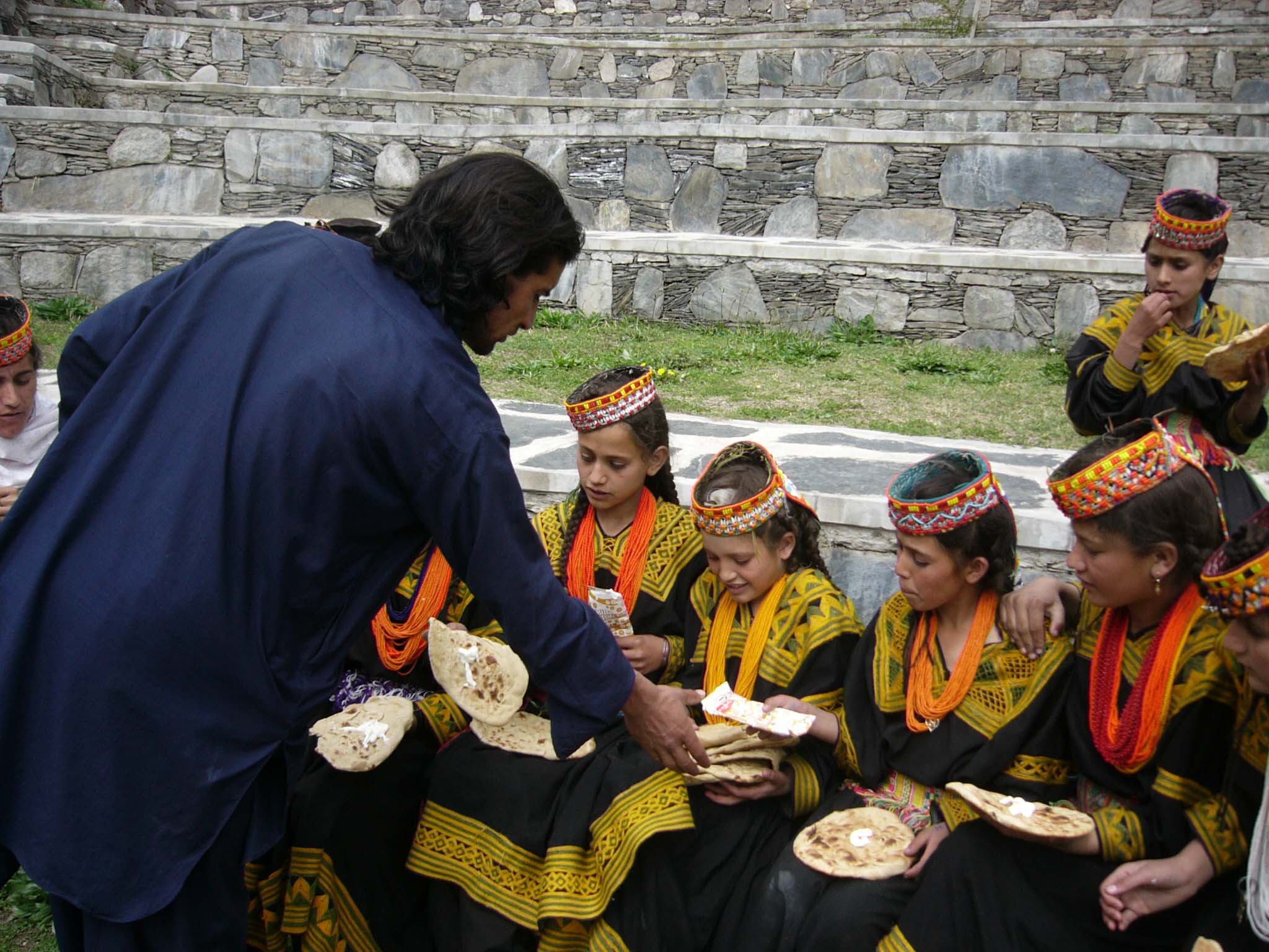 CHITRAL: A male teacher distributing Breads as Kalash girls (students) taking their lunch by butter on bread