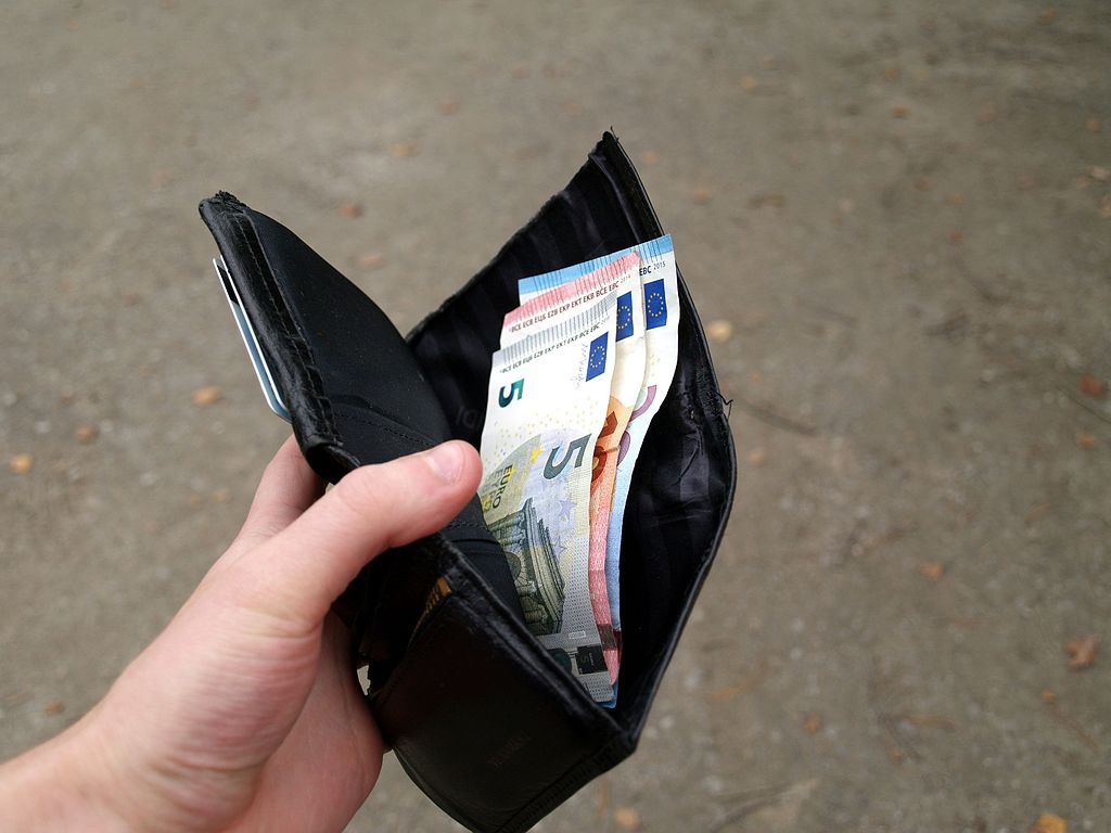 Person's hand holding a black leather wallet open, revealing a variety of Euro banknotes