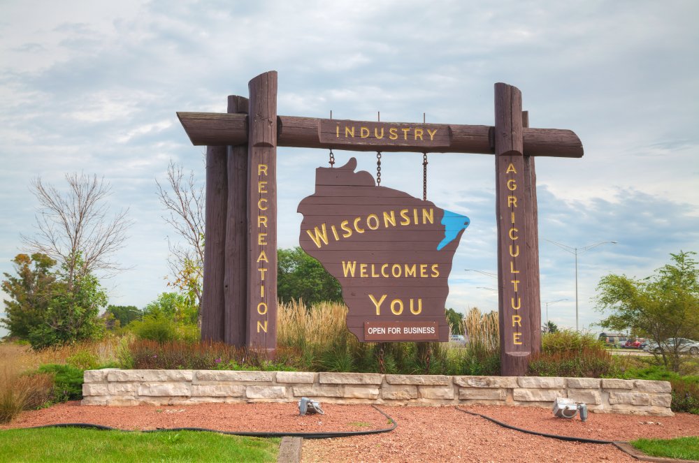 This image features a large, rustic sign welcoming visitors to Wisconsin