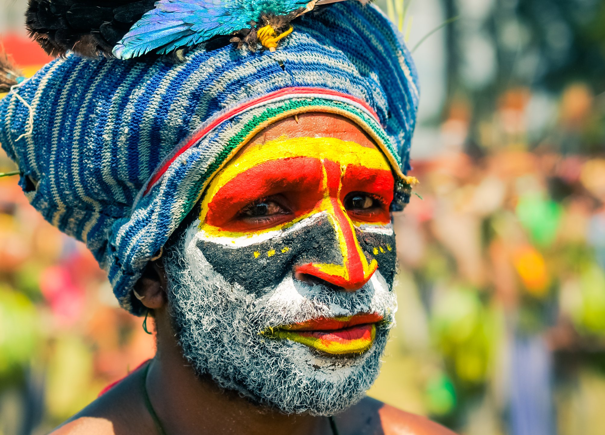 Native man with colours on his face wears blue cap with feathers