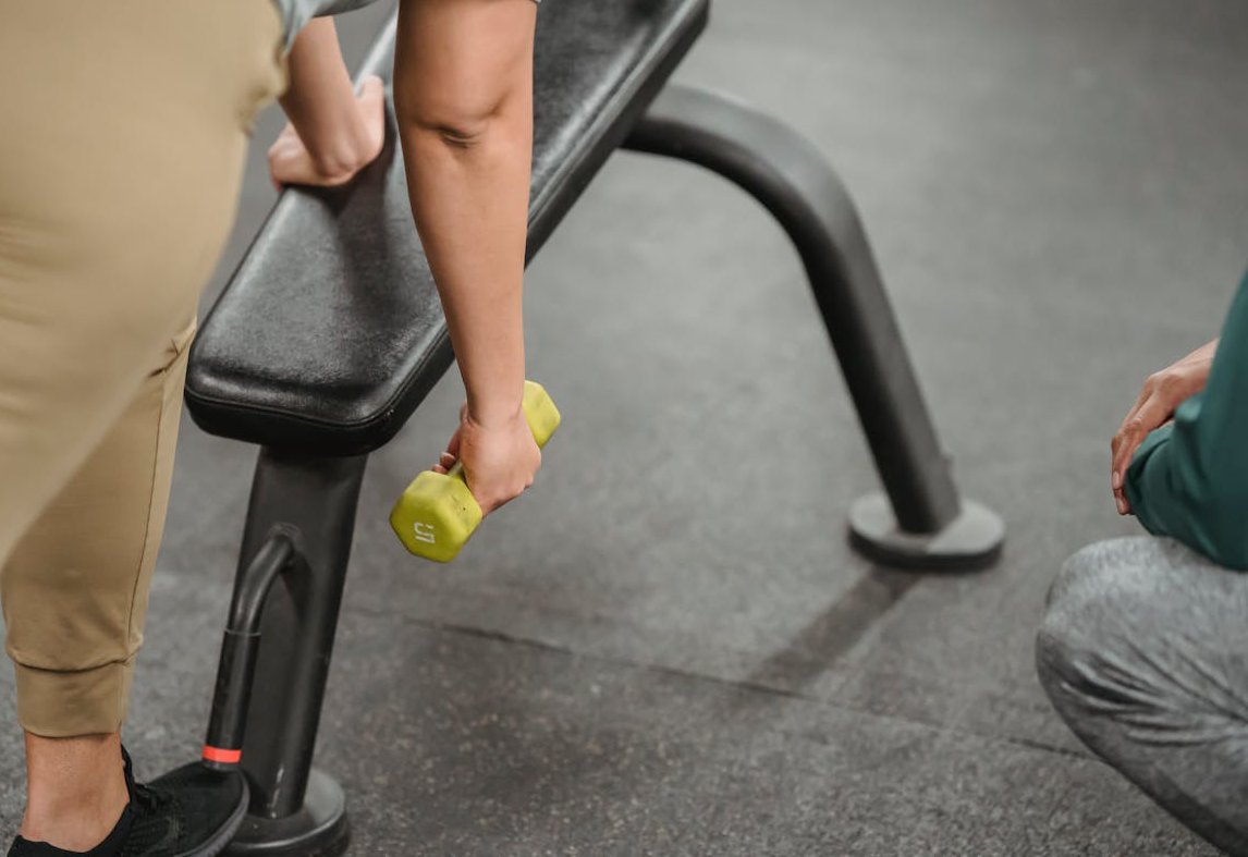 Woman lifting yellow dumbbell while her trainer watching