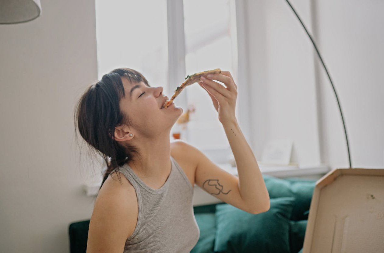 A Young Woman in Gray Tank Top Enjoying Eating Pizza