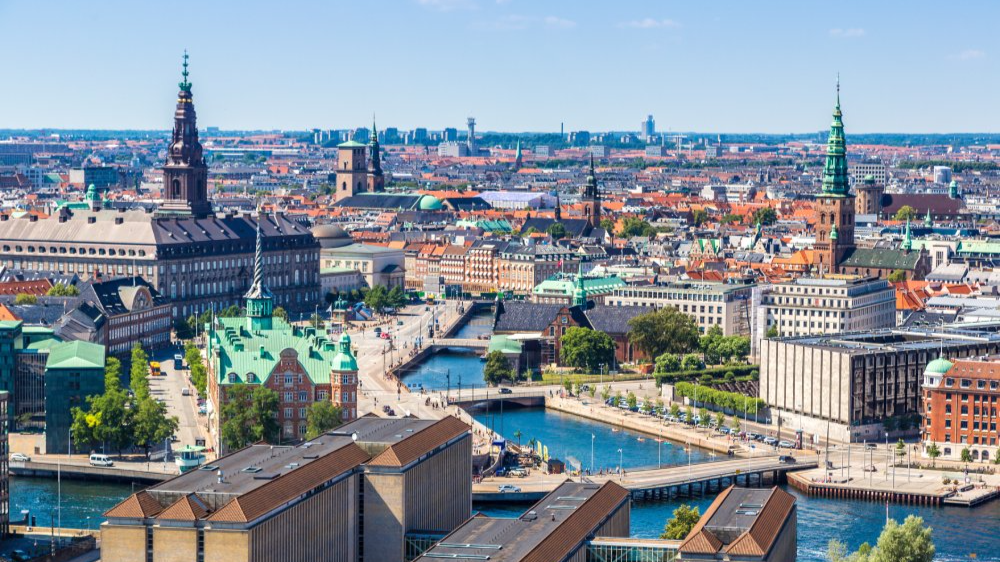 The image showcases a Vibrant urban scene of Copenhagen, Denmark captured from a high vantage point. The city appears well-developed with a mix of modern and historic architecture.
