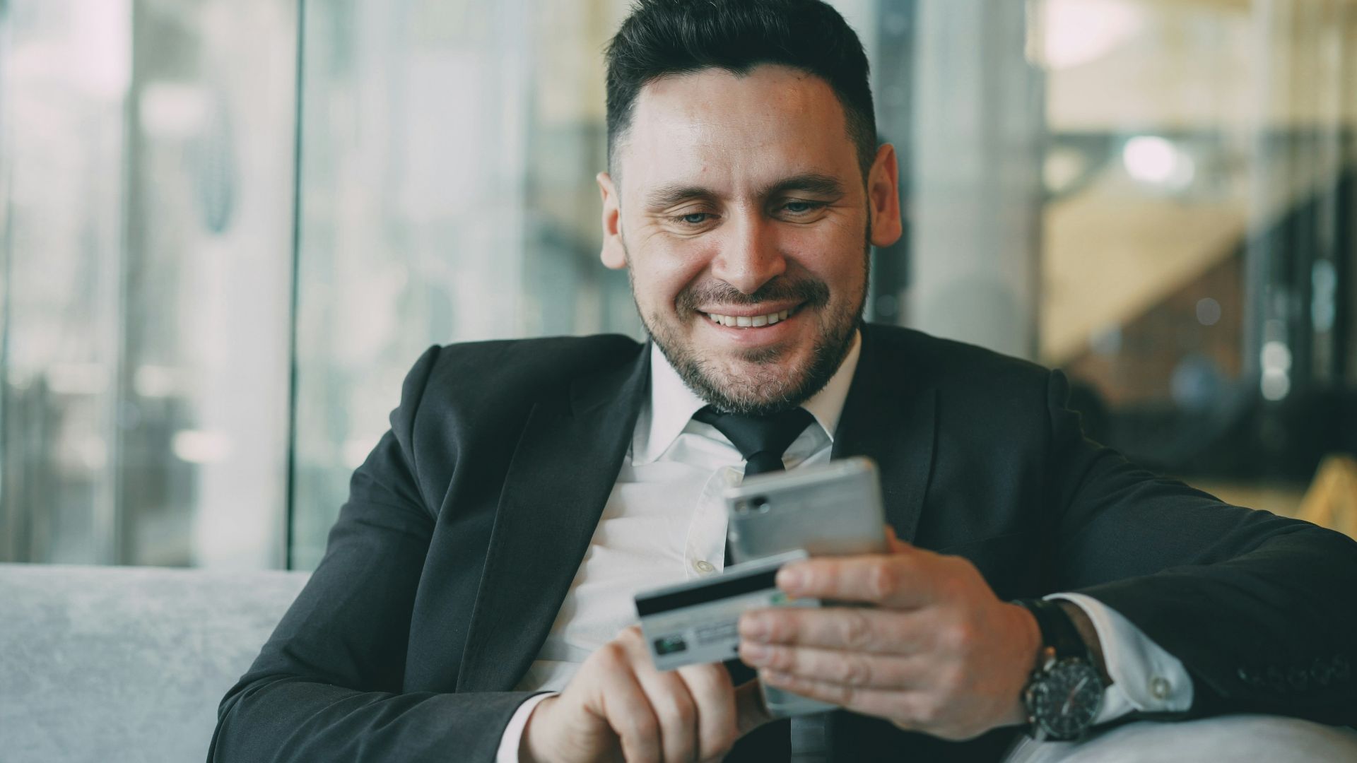 Man in suit smiling while holding phone and credit card