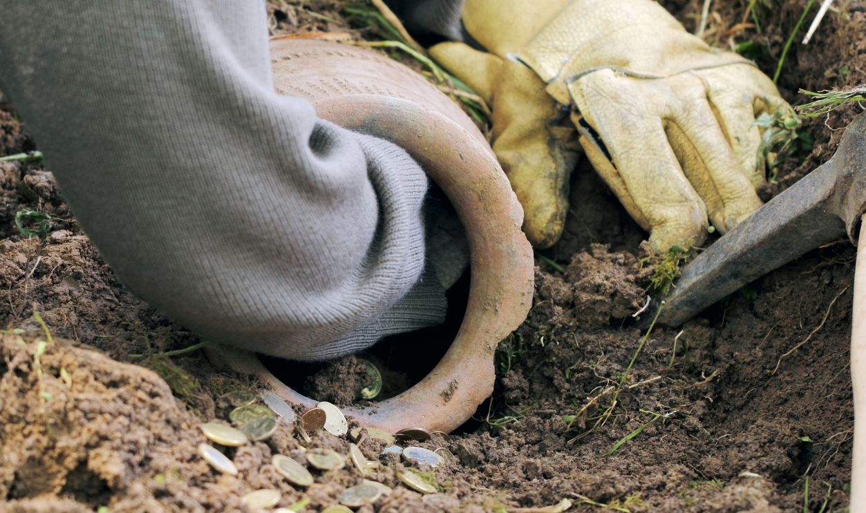 Gettyimages - 1192131698, Partly buried old clay jar with money in the land, woman is trying pick up - stock photo Partly buried old clay jar with money in the land, woman is trying pick up