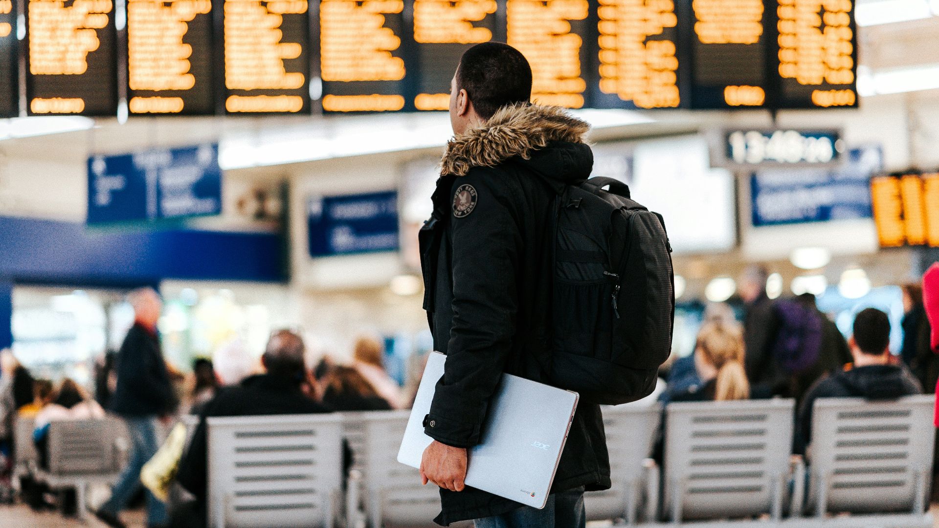 man standing inside airport looking at LED flight schedule bulletin board