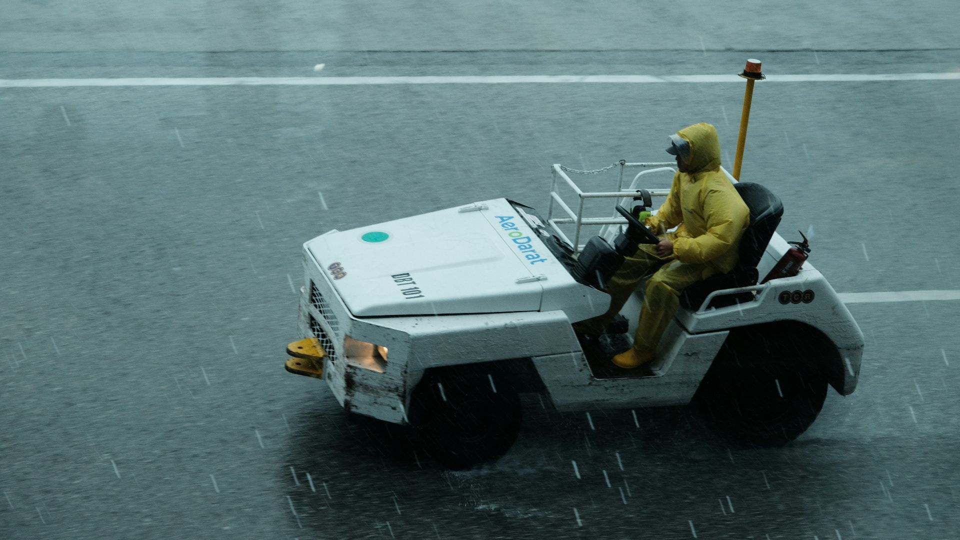 A man in a yellow rain suit driving a white vehicle