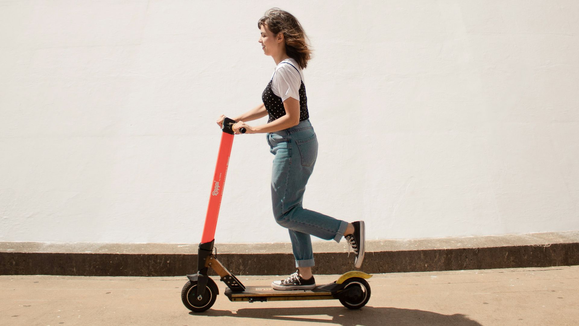 woman in white shirt and blue denim jeans riding red and black kick scooter