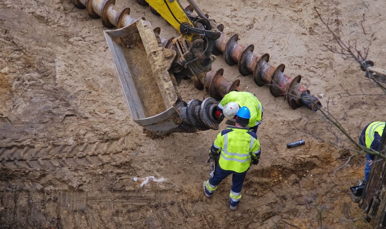 Oil and Gas Mining Company Construction Workers Preparing Long Industrial Drill For Pile Driver Machine