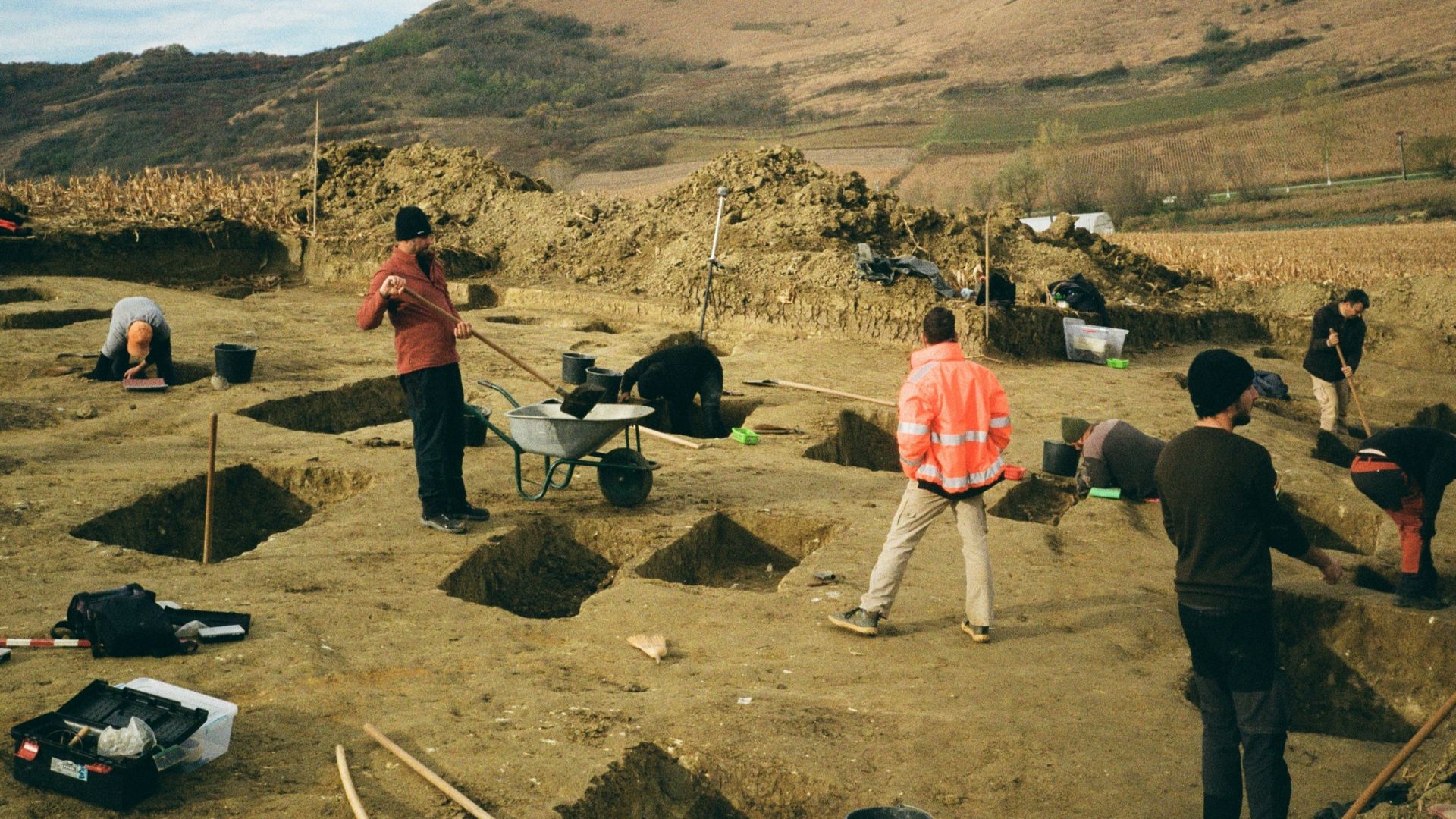 Archaeologists excavating a field with tools and trenches.