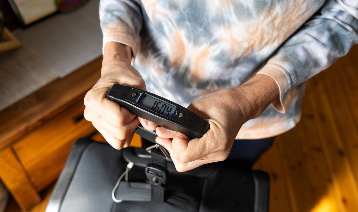 Closeup of woman weighing luggage with a digital weighing scale to ascertain luggage weight before travel by air