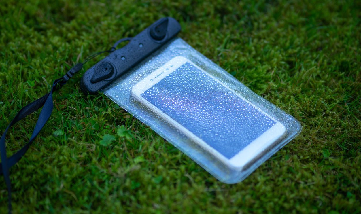 Smartphone in a waterproof case on the green grass. Means to prevent moisture from entering the phone. A plastic case for a smartphone when traveling and on vacation.