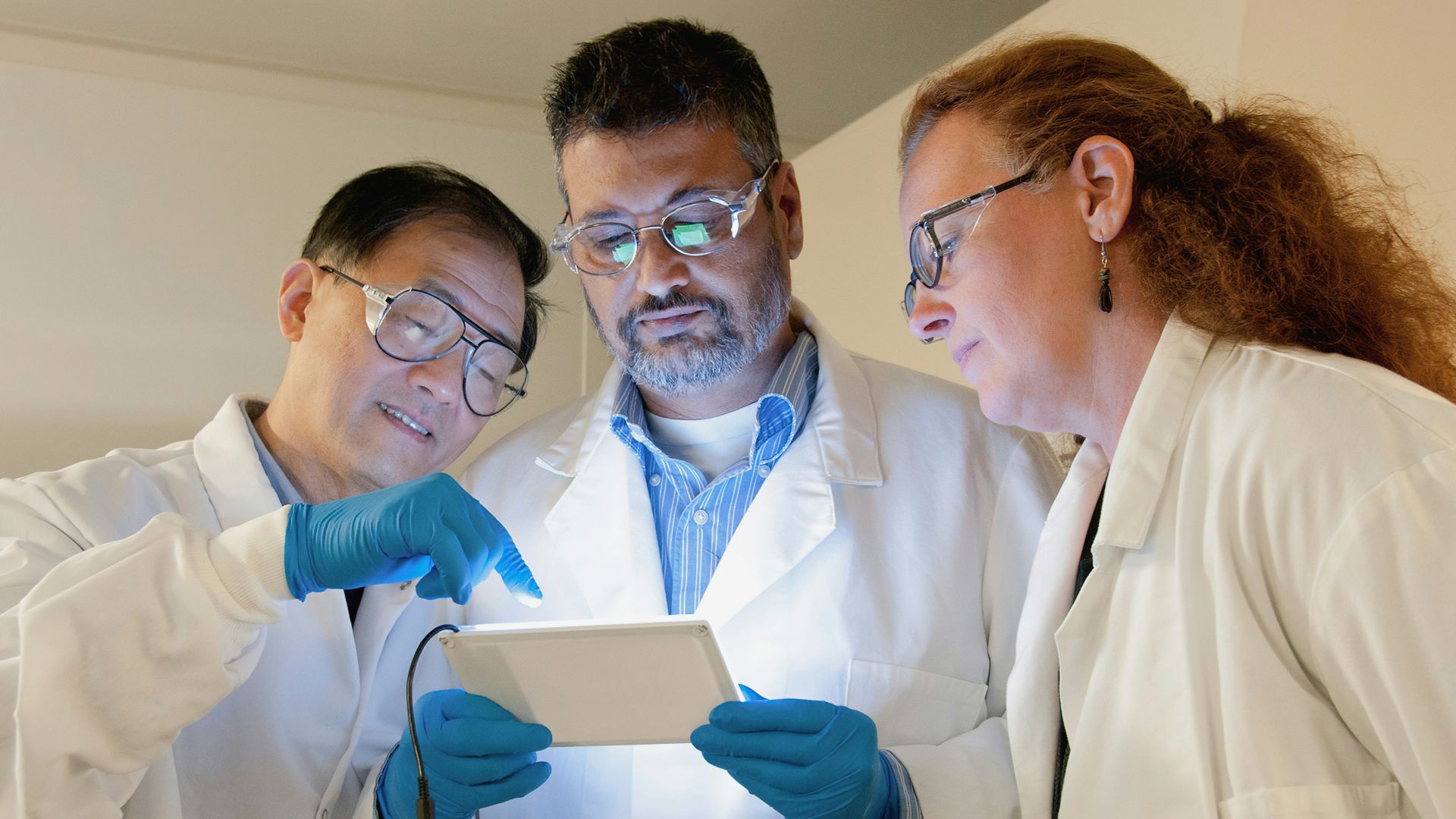 three people in lab coats looking at a tablet