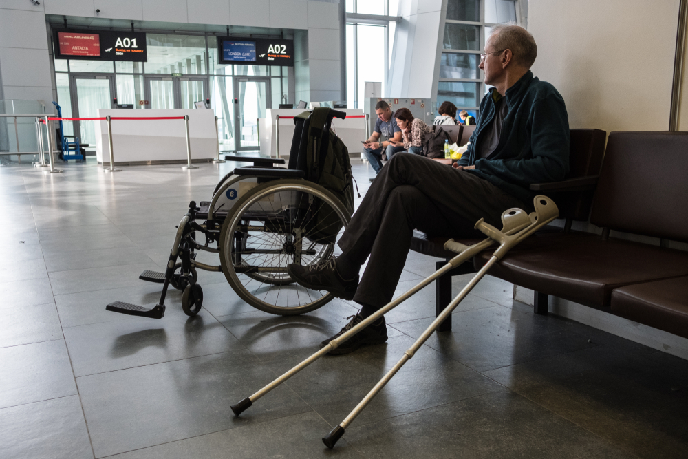 An elderly bald  person with crutch at airport.